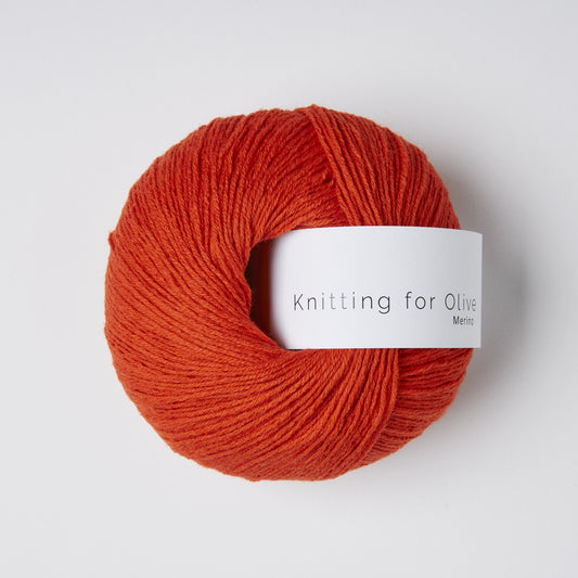 Ball of blood orange colored merino fingering yarn with a white Knitting for Olive brand label
