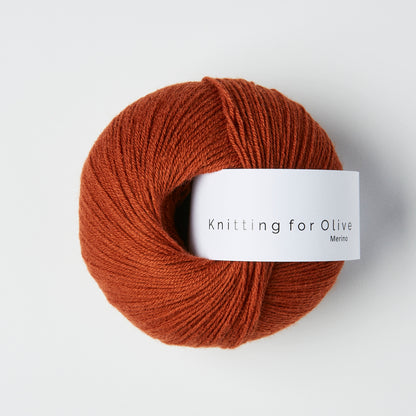 Ball of rust colored merino fingering yarn with a white Knitting for Olive brand label